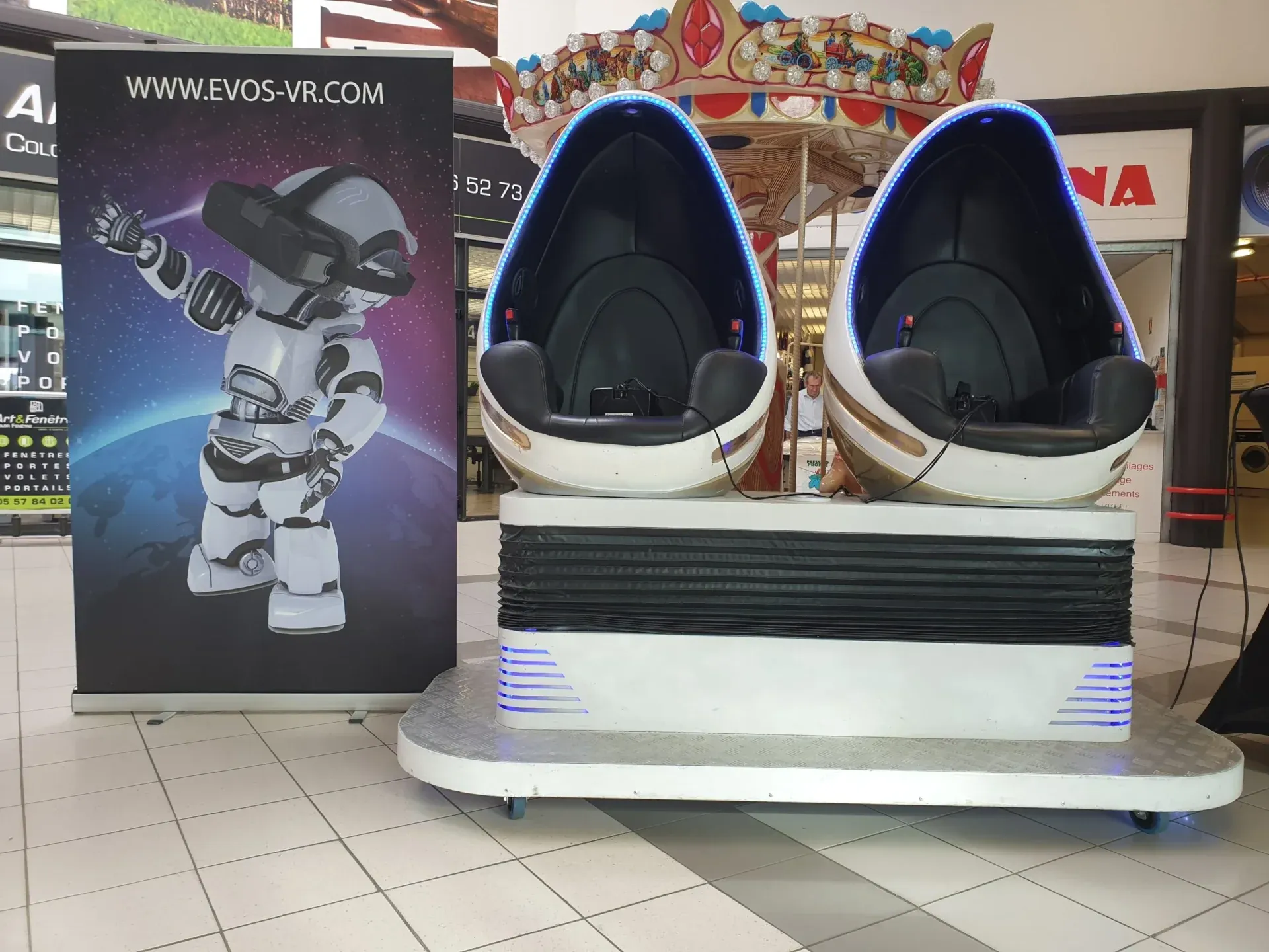 Deux capsules VR en forme d'oeuf blanches avec LED bleues et bannière Evos installées dans un centre commercial