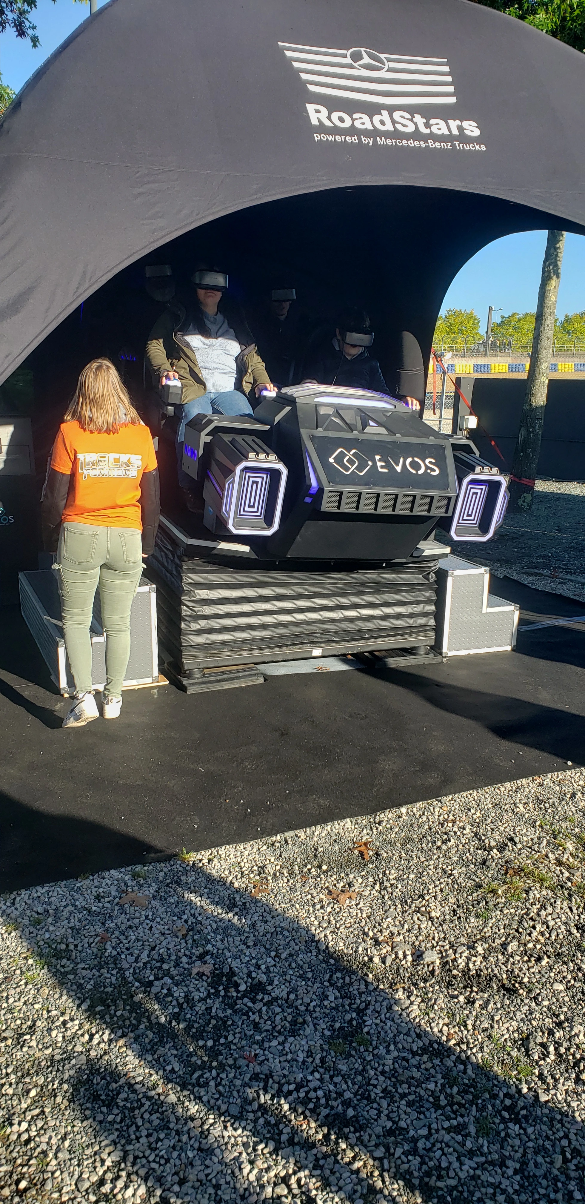 Animateur en t-shirt orange accompagnant un visiteur sur la navette VR aux couleurs By Evos