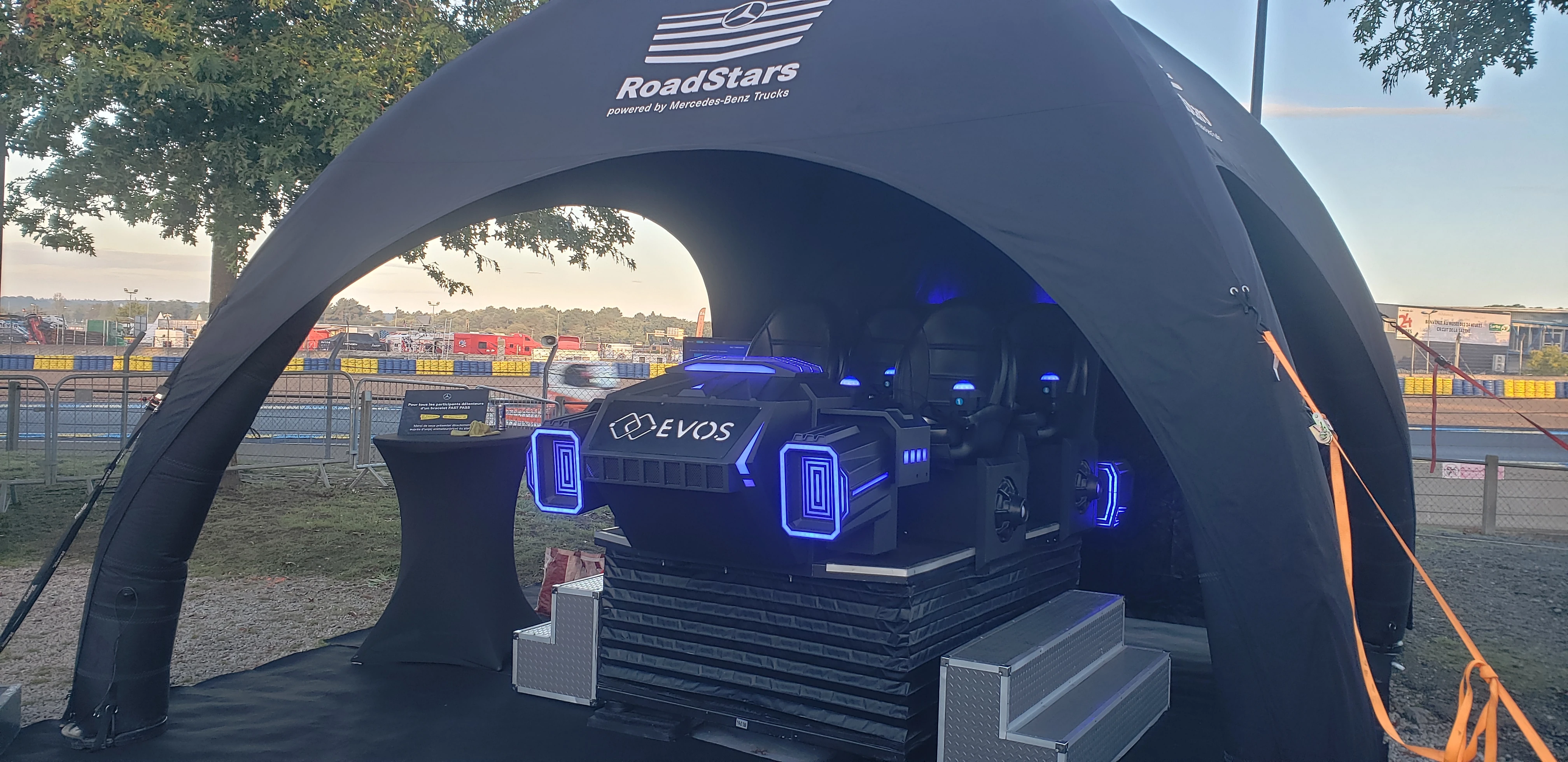 Simulateur navette 4 places avec branding EVOS lumineux bleu sous tente sponsor sur le paddock