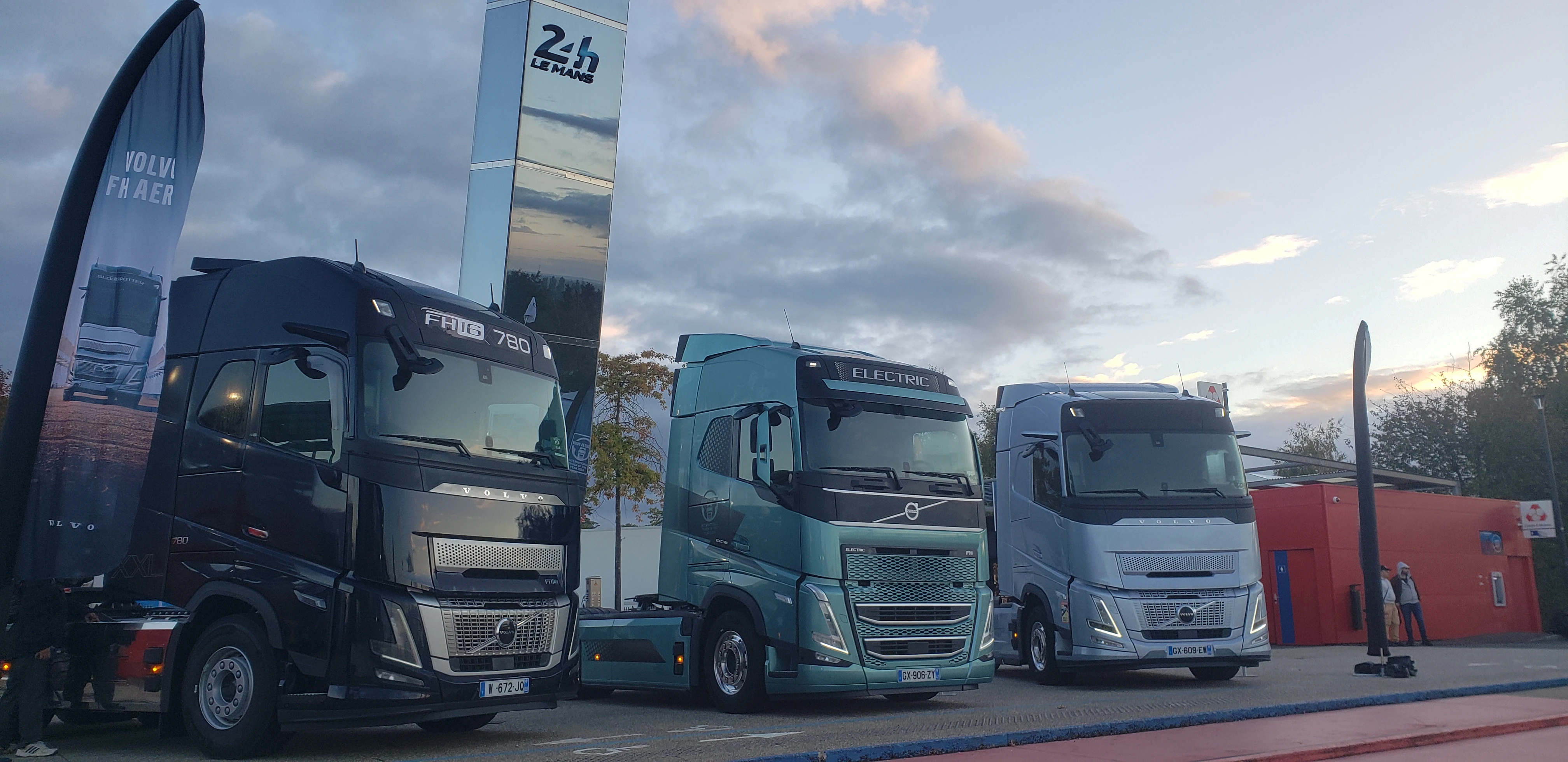 Trois camions Volvo FH16 780 Electric et FH alignés devant le totem 24h Le Mans au lever du soleil