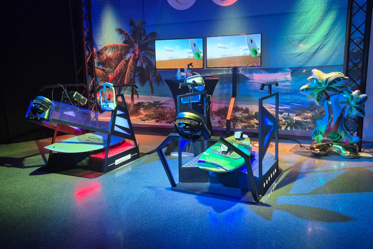Trois simulateurs de surf VR alignés avec écrans et décor tropical