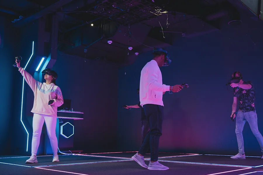Trois joueurs avec casques VR et manettes dans une salle d'escape game éclairée au néon