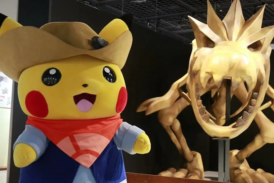 Mascotte Pikachu en tenue d'explorateur à côté d'une réplique de fossile Pokémon lors de l'exposition