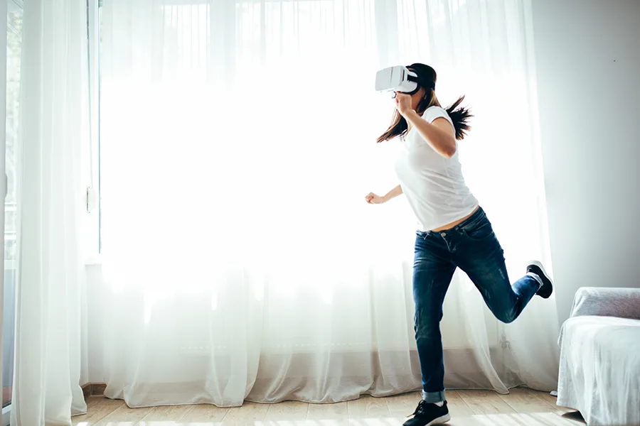 Femme debout avec un casque de réalité virtuelle dans un salon lumineux