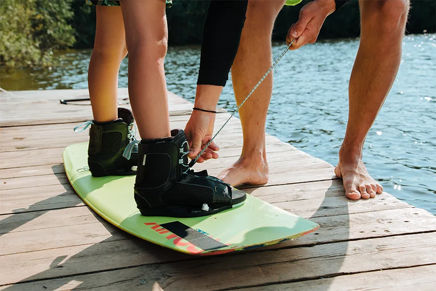 Rider chaussant ses fixations de wakeboard sur un ponton au bord d'un lac