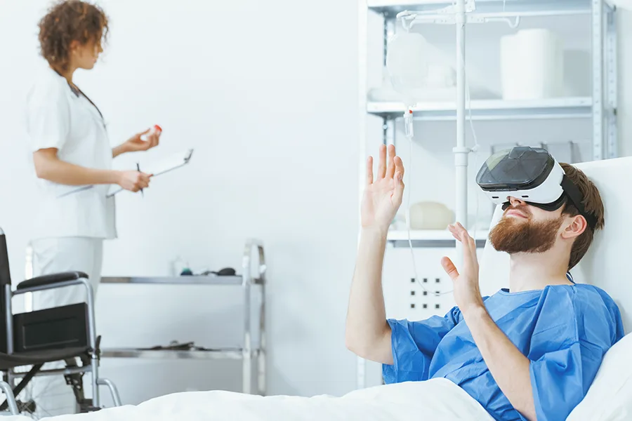 Patient hospitalisé portant un casque VR les mains levées, infirmière en arrière-plan