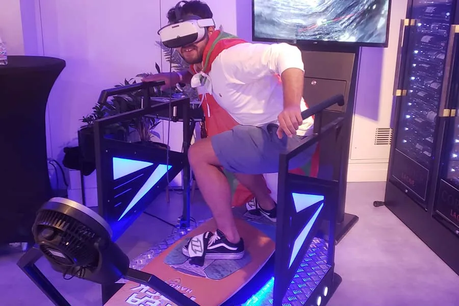 Participant sur un simulateur de surf VR avec casque et écran de retransmission
