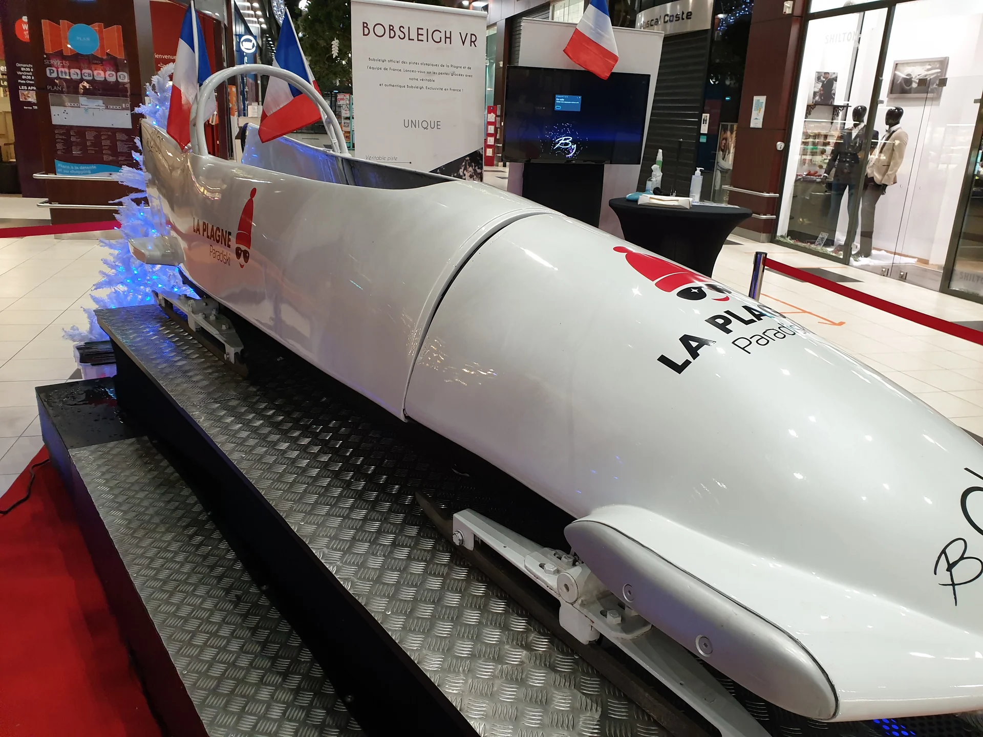 Détail de la coque arrière du bobsleigh VR avec logo La Plagne devant le kakémono explicatif et la galerie en arrière-plan