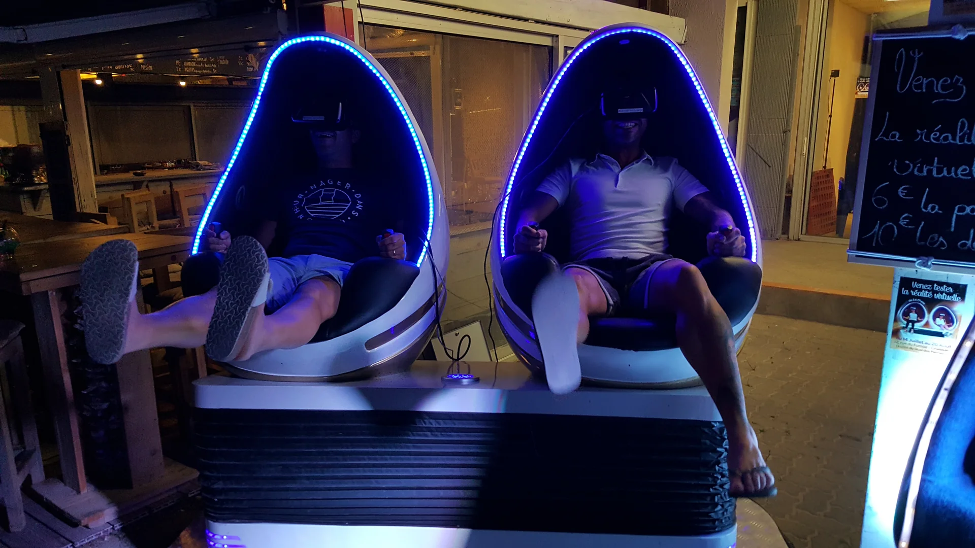 Deux adultes en short et tongs en pleine session sur les fauteuils Evos Sensation casques VR posés