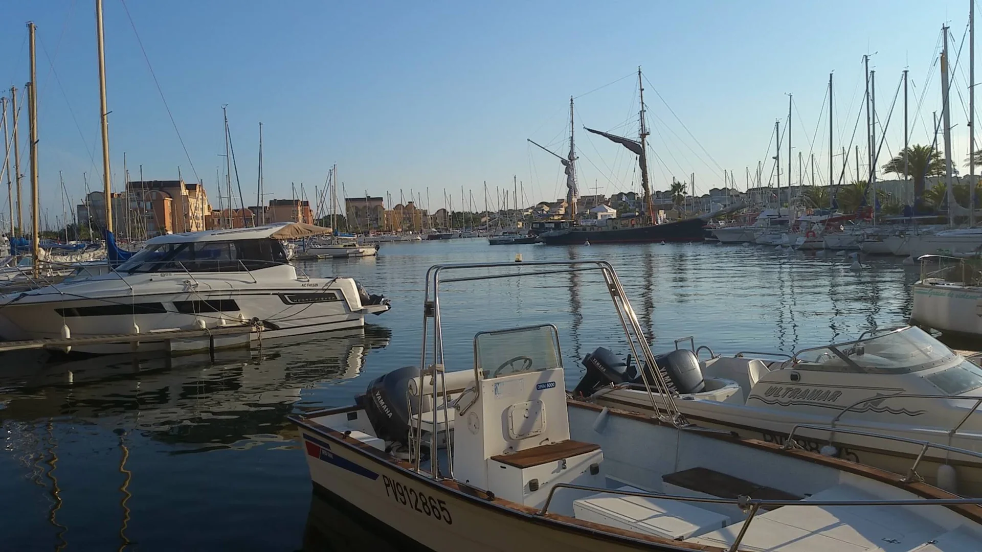 Vue du port de Gruissan avec voiliers amarrés et grand-voilier à proximité du Quai des Palmiers en fin de journée
