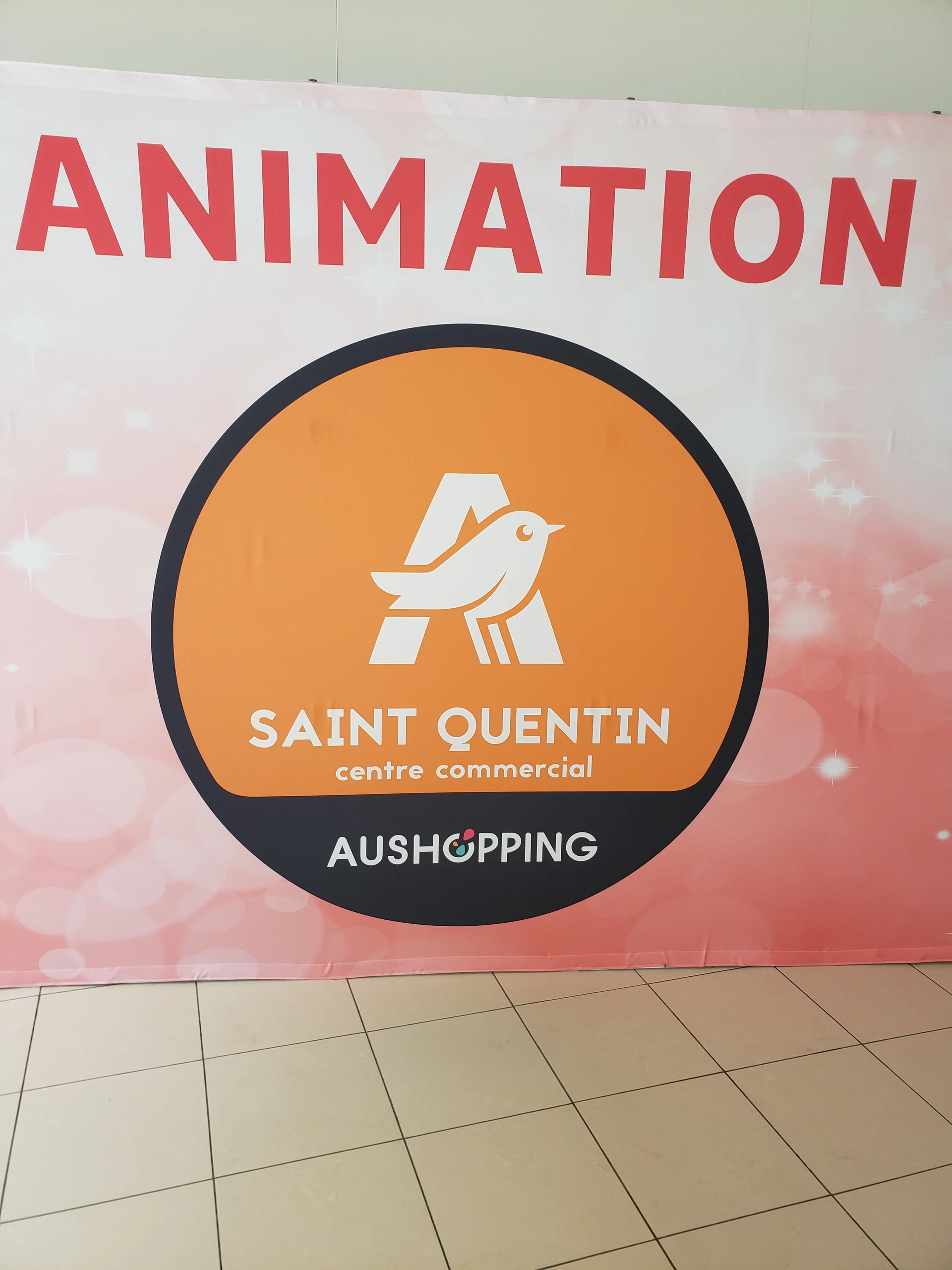 Kakemono officiel du centre commercial Aushopping Saint-Quentin avec logo orange en bord de zone d'animation
