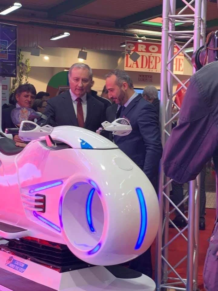 Élu toulousain en costume examinant le simulateur moto VR sur stand La Dépêche du Midi à la Foire de Toulouse 2019