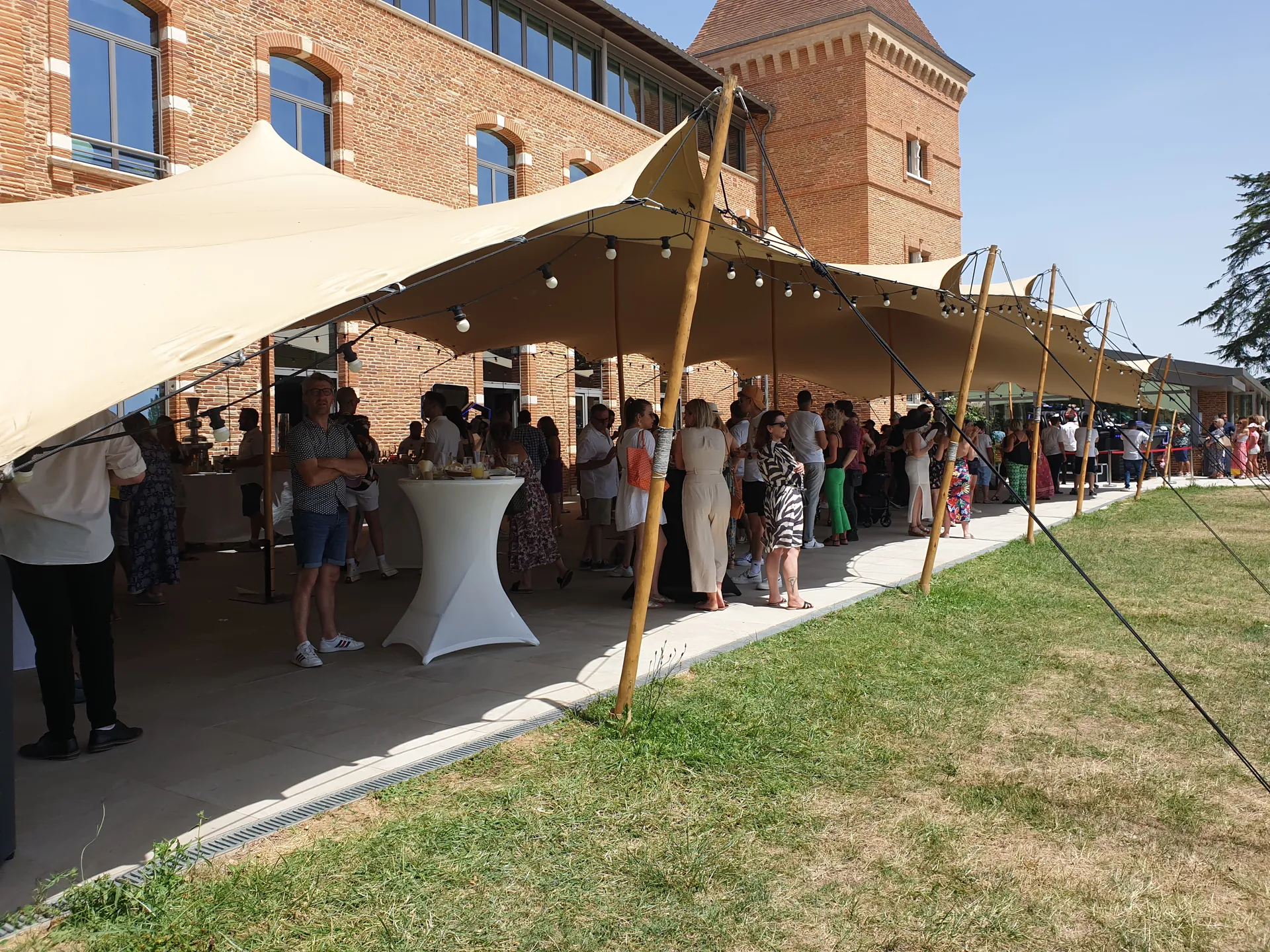 Tente nomade crème devant la façade brique du Domaine de Preissac avec foule en tenue cocktail