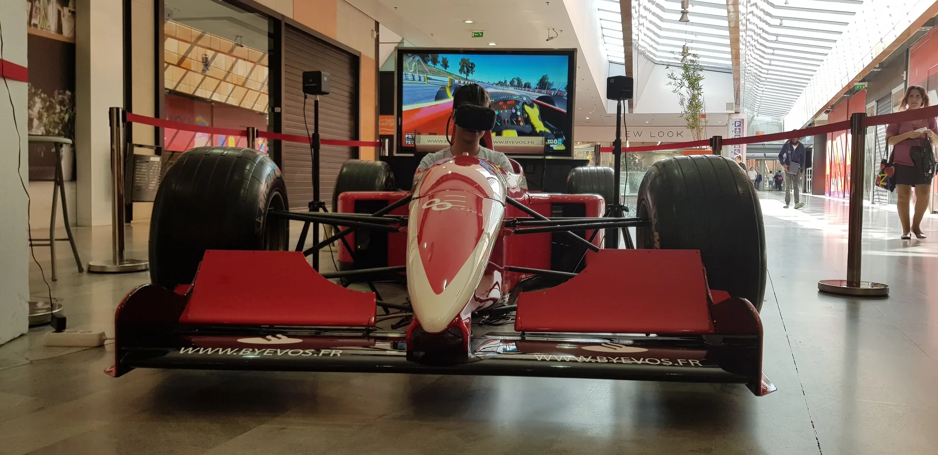 Simulateur F1 VR avec écran TV diffusant la course en direct dans la galerie marchande Espace Saint-Georges