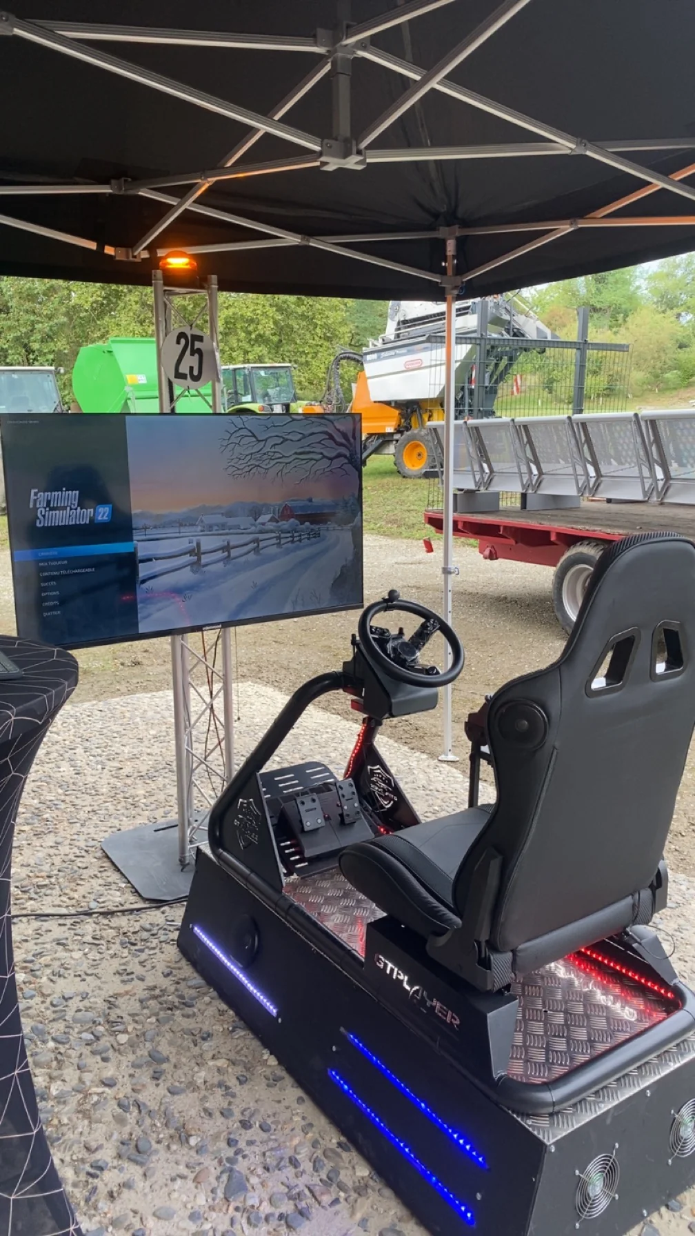 Simulateur de conduite agricole avec volant et écran Farming Simulator sous un barnum lors d'un salon en plein air