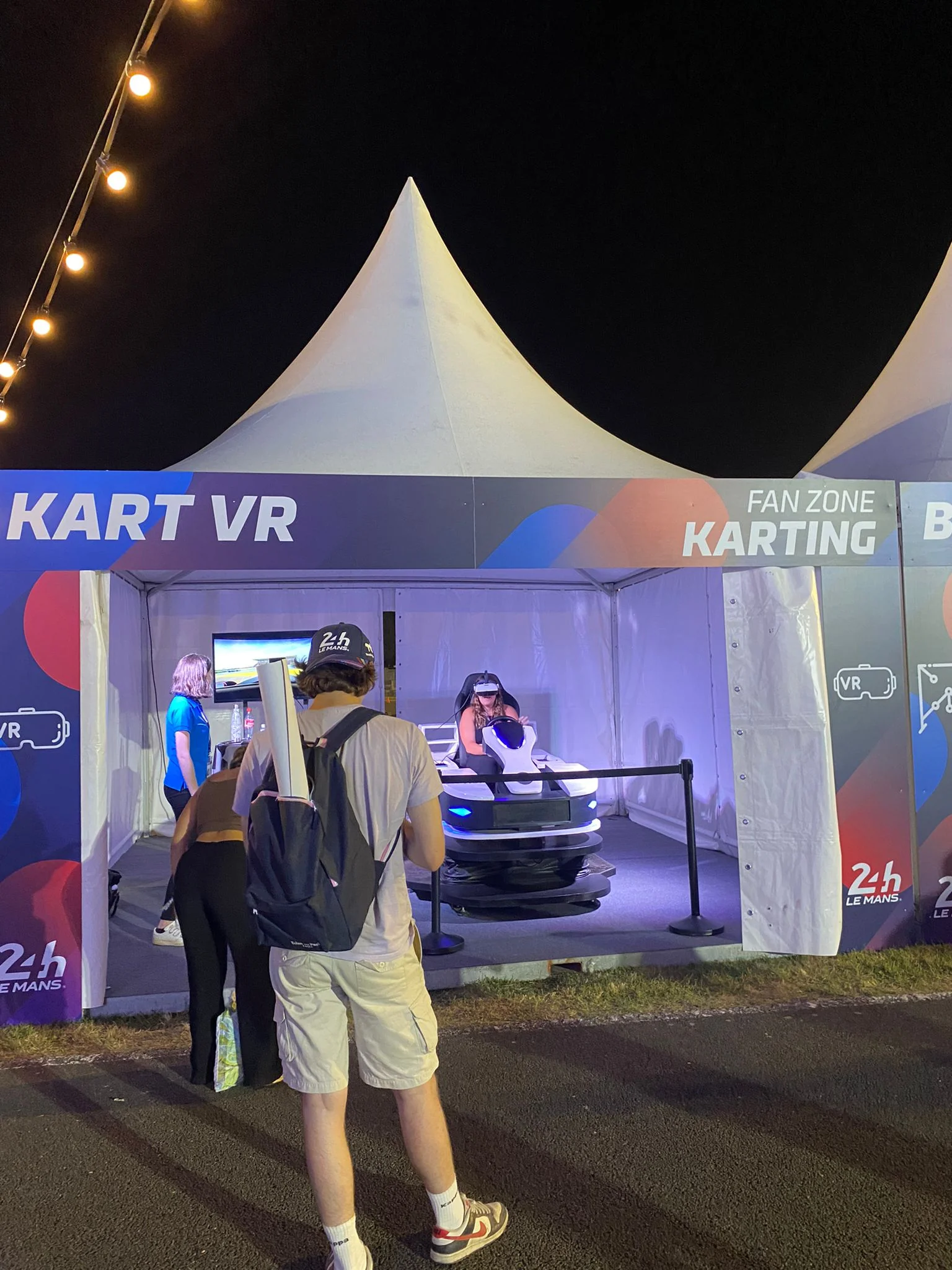 Visiteurs devant le stand Kart VR illuminé de nuit aux 24h du Mans