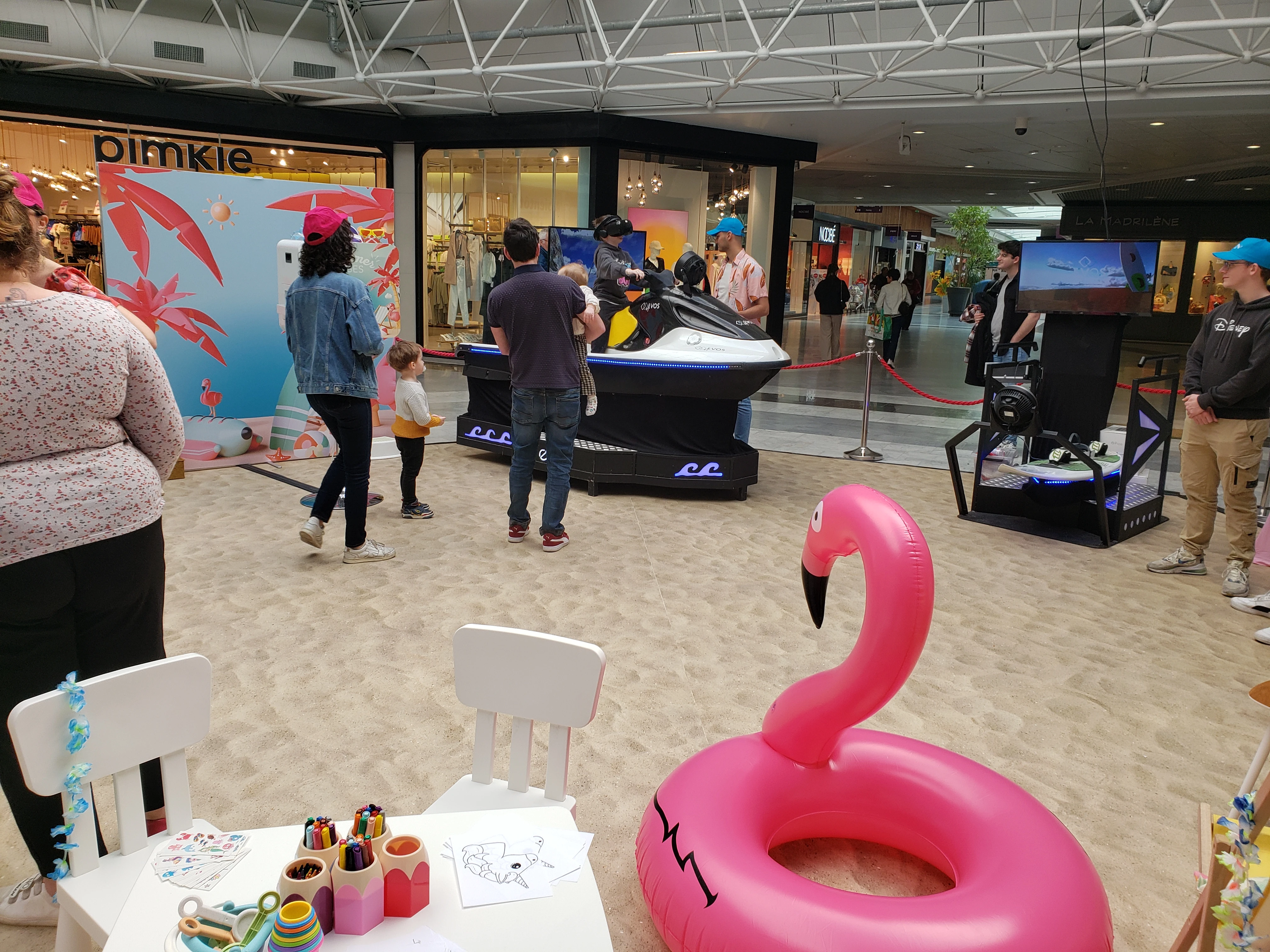 Bouée gonflable flamant rose au centre de la zone Summer Vibes avec atelier coloriage enfants et jet ski VR en arrière-plan