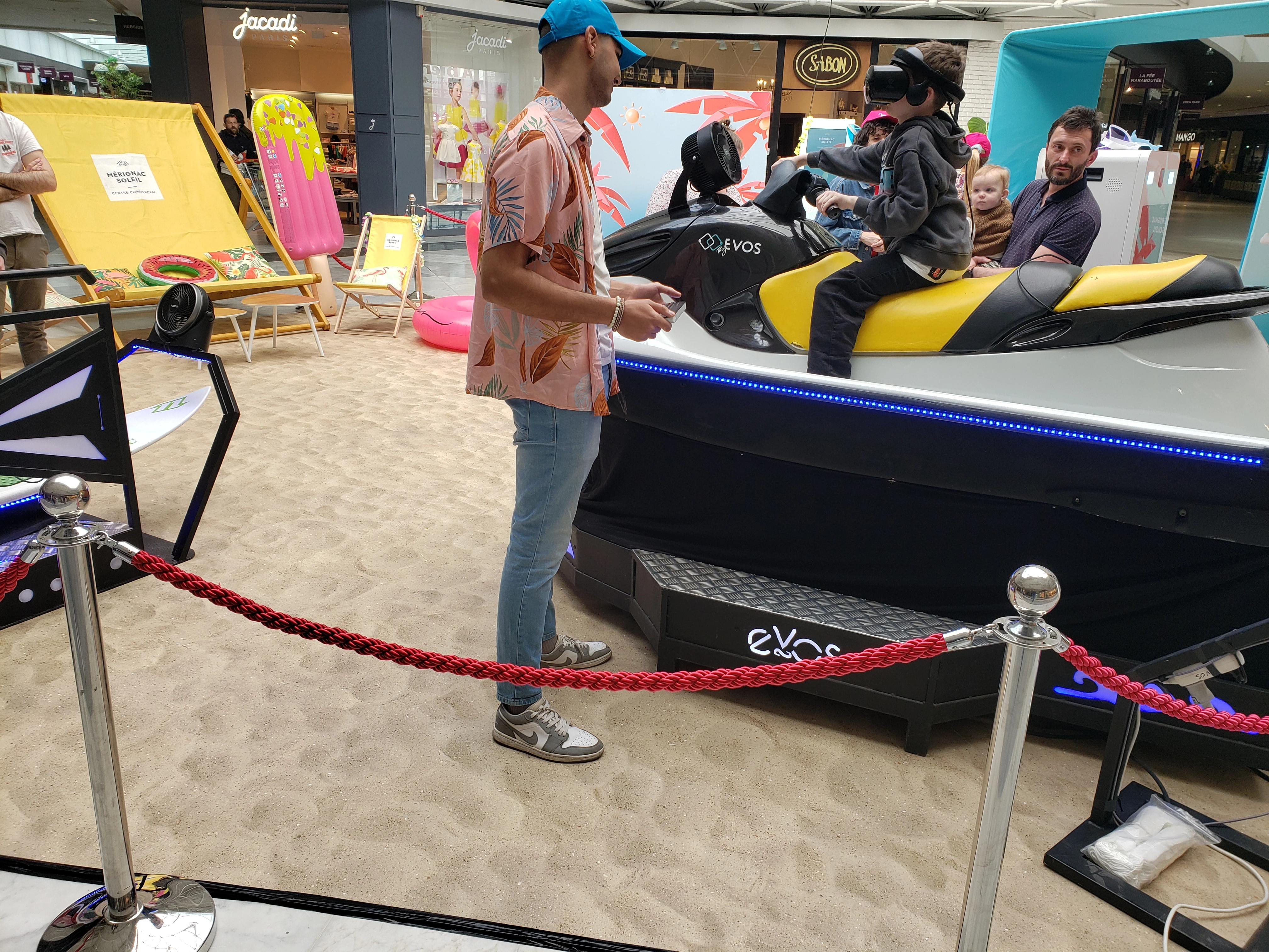 Jeune participant casque VR sur le jet ski accompagné par sa famille devant la boutique Jacadi