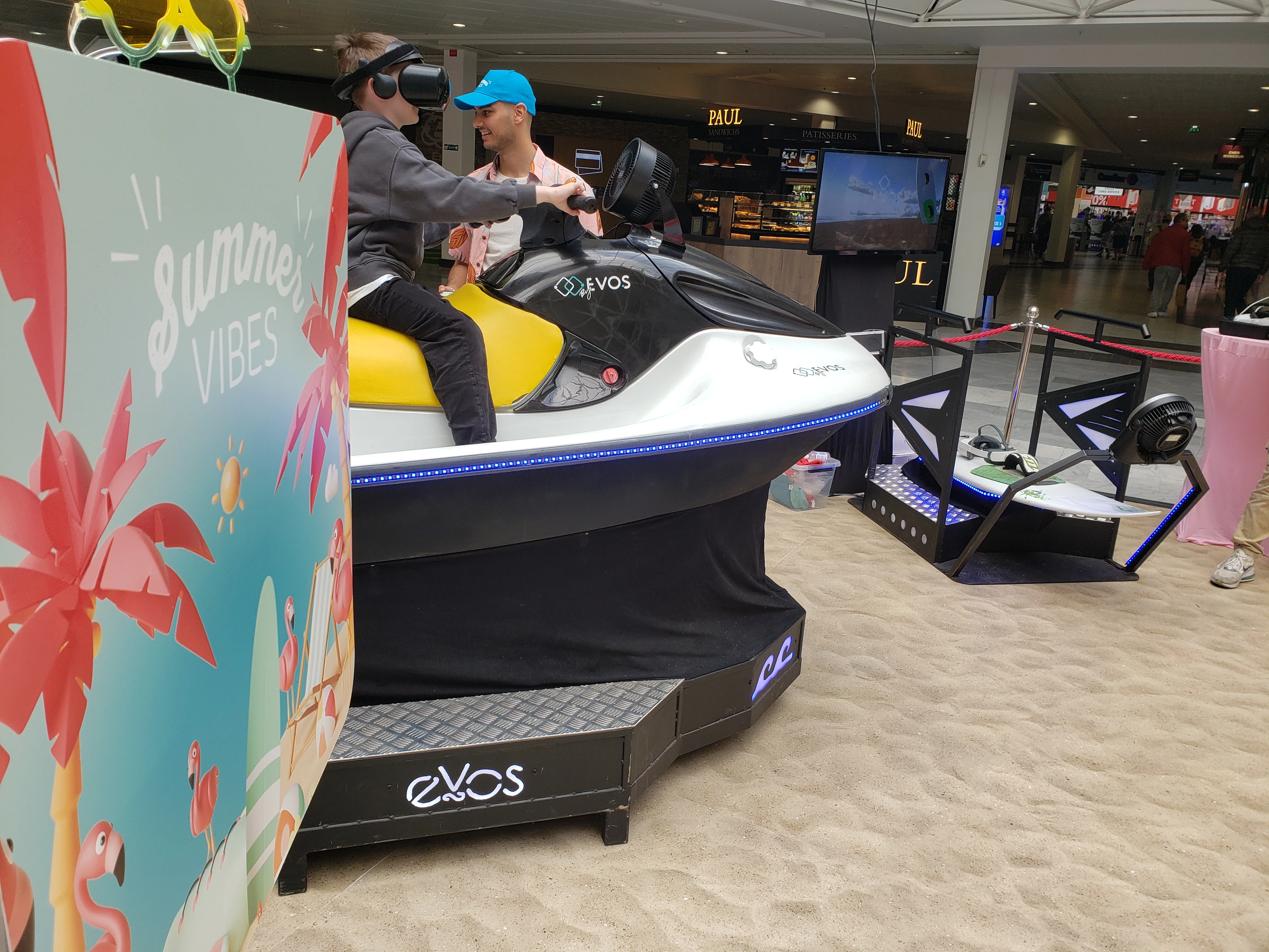 Simulateur jet ski VR au premier plan et simulateur surf VR sur plateforme dynamique en face de la boulangerie PAUL