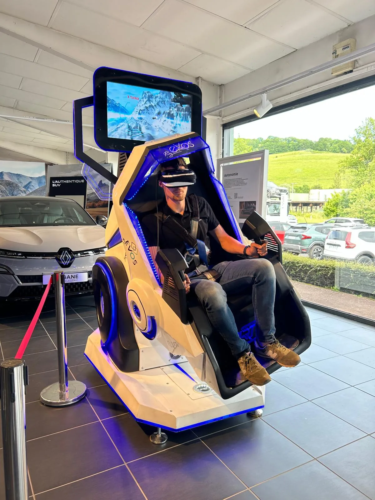Participant adulte sanglé dans le Double 360 VR avec Renault Megane visible en arrière-plan du showroom