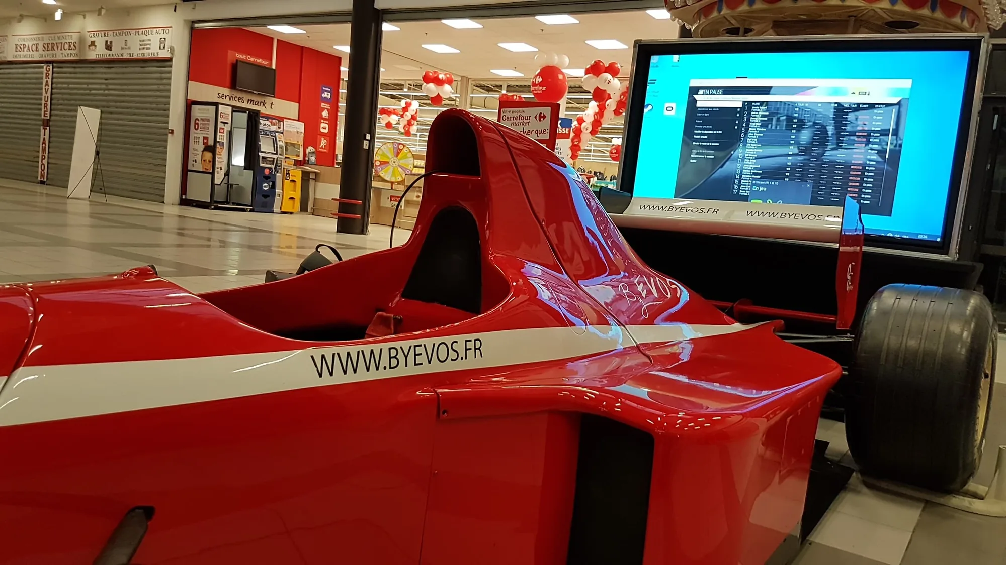Arrière du baquet du simulateur de Formule 1 VR, marquage byevos.fr et écran de retransmission