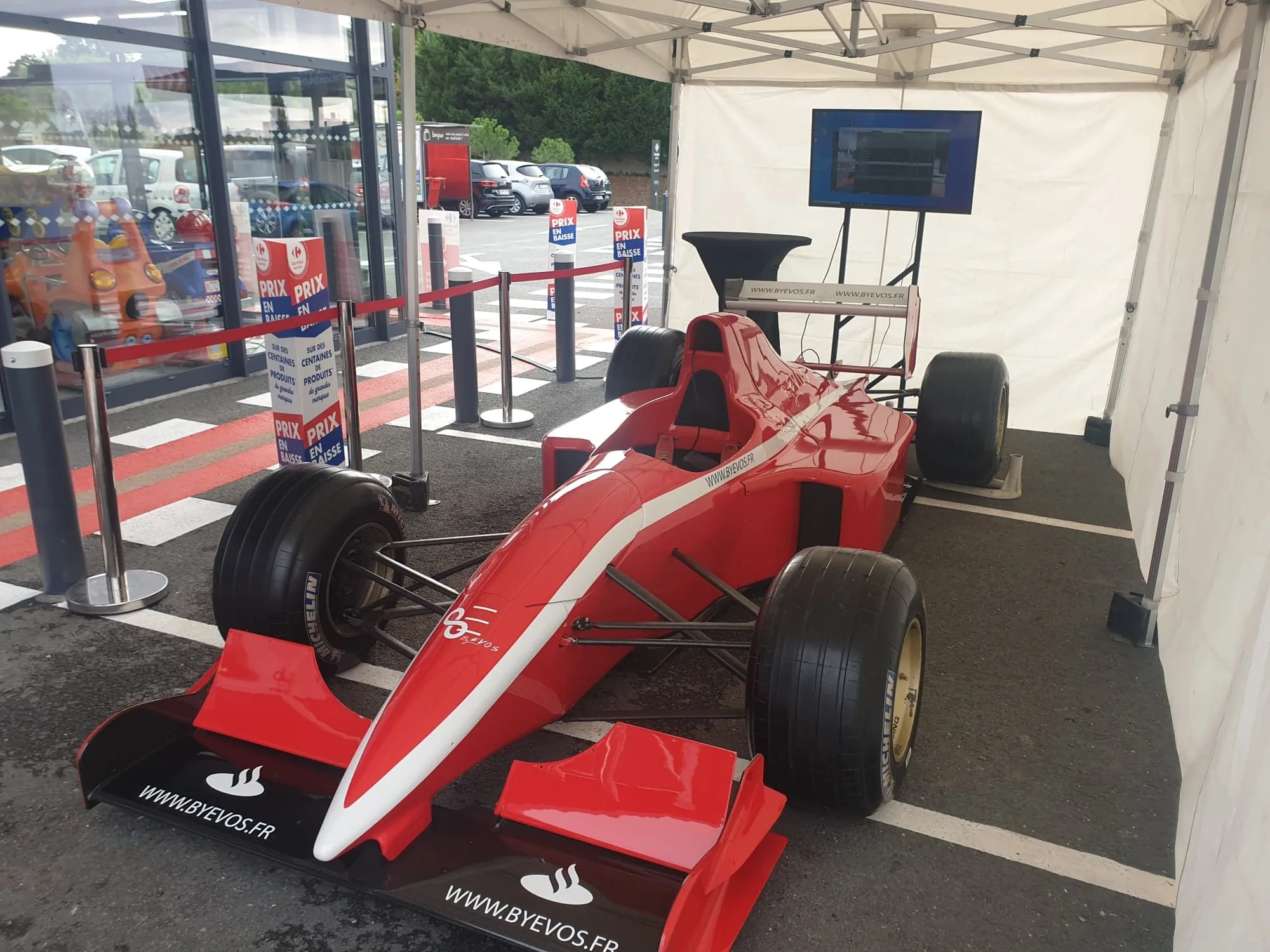 Monoplace rouge du simulateur F1 VR sous tente, aileron portant l'adresse byevos.fr