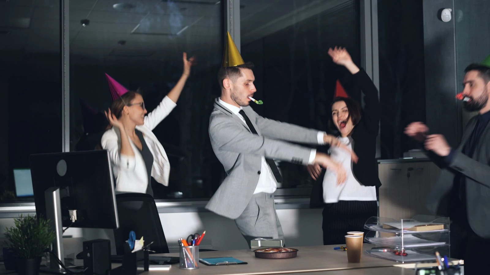 Collègues coiffés de chapeaux de fête soufflant dans des cotillons à une soirée de bureau