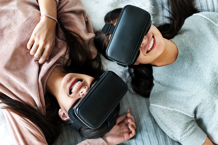Deux jeunes filles allongées sur un lit, vues en contre-plongée, portant des casques de réalité virtuelle.