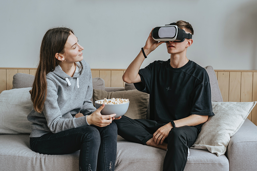 Deux amis essayant un casque de réalité virtuelle, une femme tenant un bol de pop-corn et un homme portant le casque et vivant une expérience de réalité virtuelle.